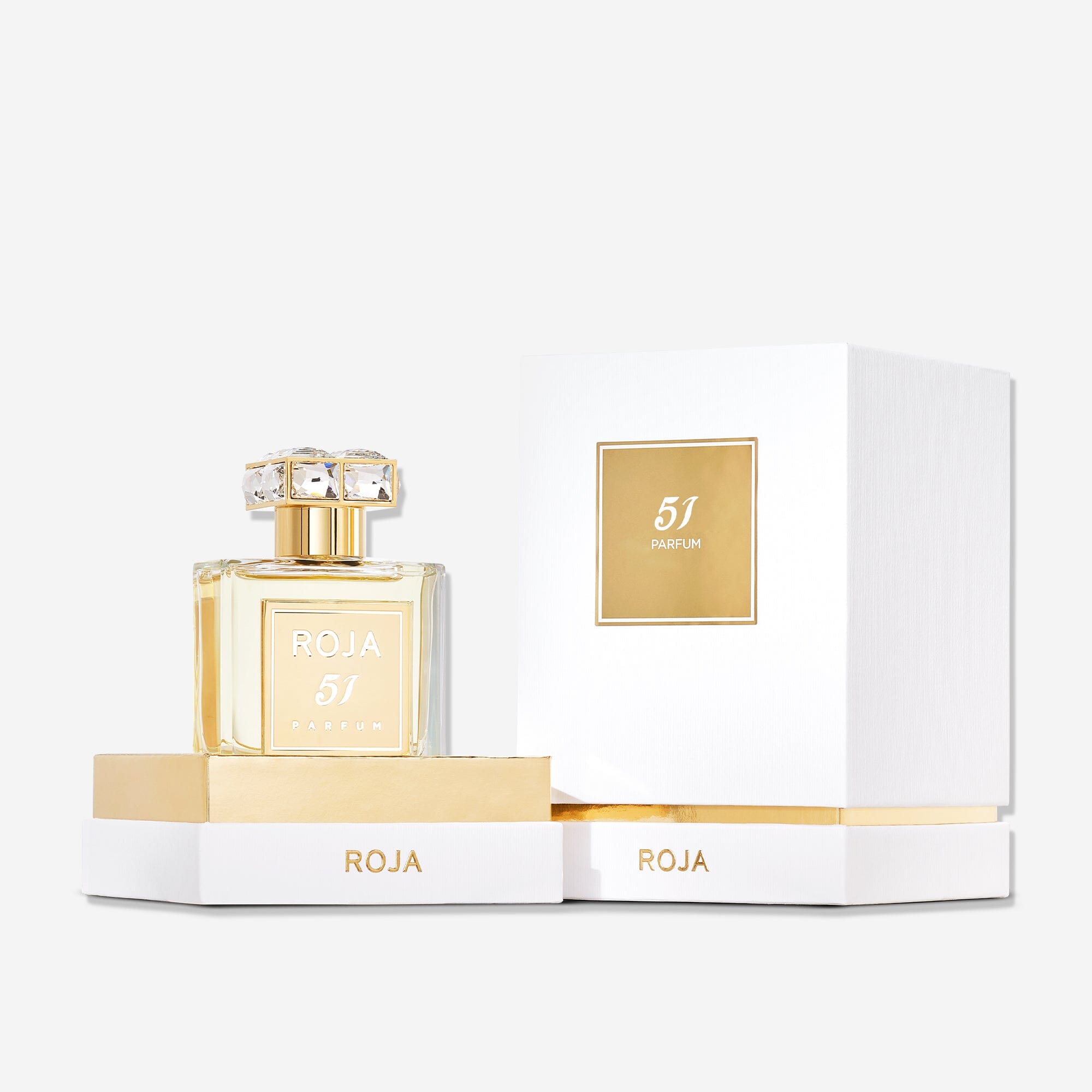 A bottle of Roja Parfums 51 Pour Femme with a gold label is displayed beside its open white and gold box on a white background, reflecting the elegance of Mayfair London.