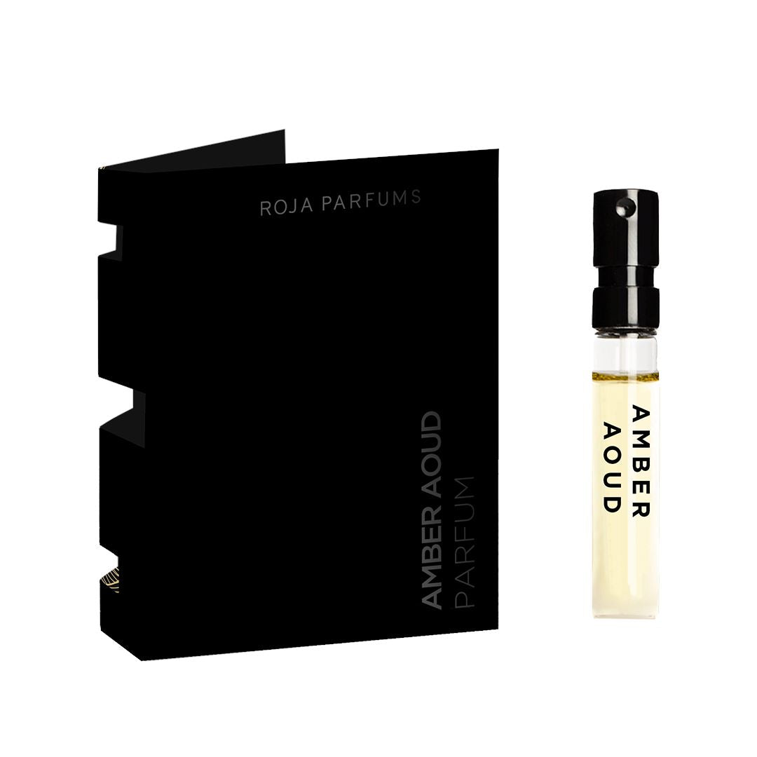 A small sample spray vial labeled Amber Aoud Sample (Gift) is next to a black folded card packaging that reads Roja Parfums.