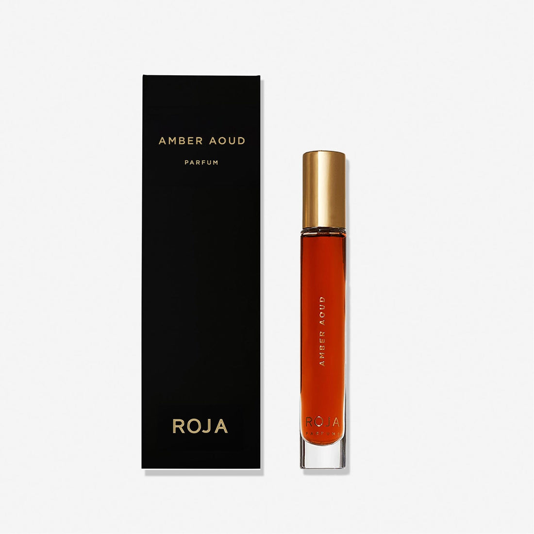 A tall, slim glass bottle of Roja Parfums Amber Aoud with a gold cap stands beside a sleek black box adorned with gold text—an elegant display against a plain white background.