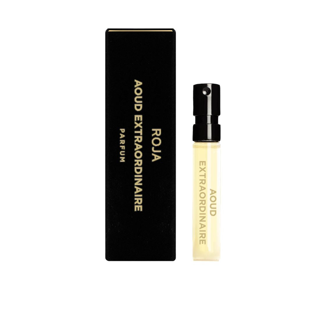 A small clear spray vial labeled "Aoud Extraordinaire Sample (Gift)" by Roja Parfums stands next to a sleek black box with gold text reading "Roja Aoud Extraordinaire Parfum.