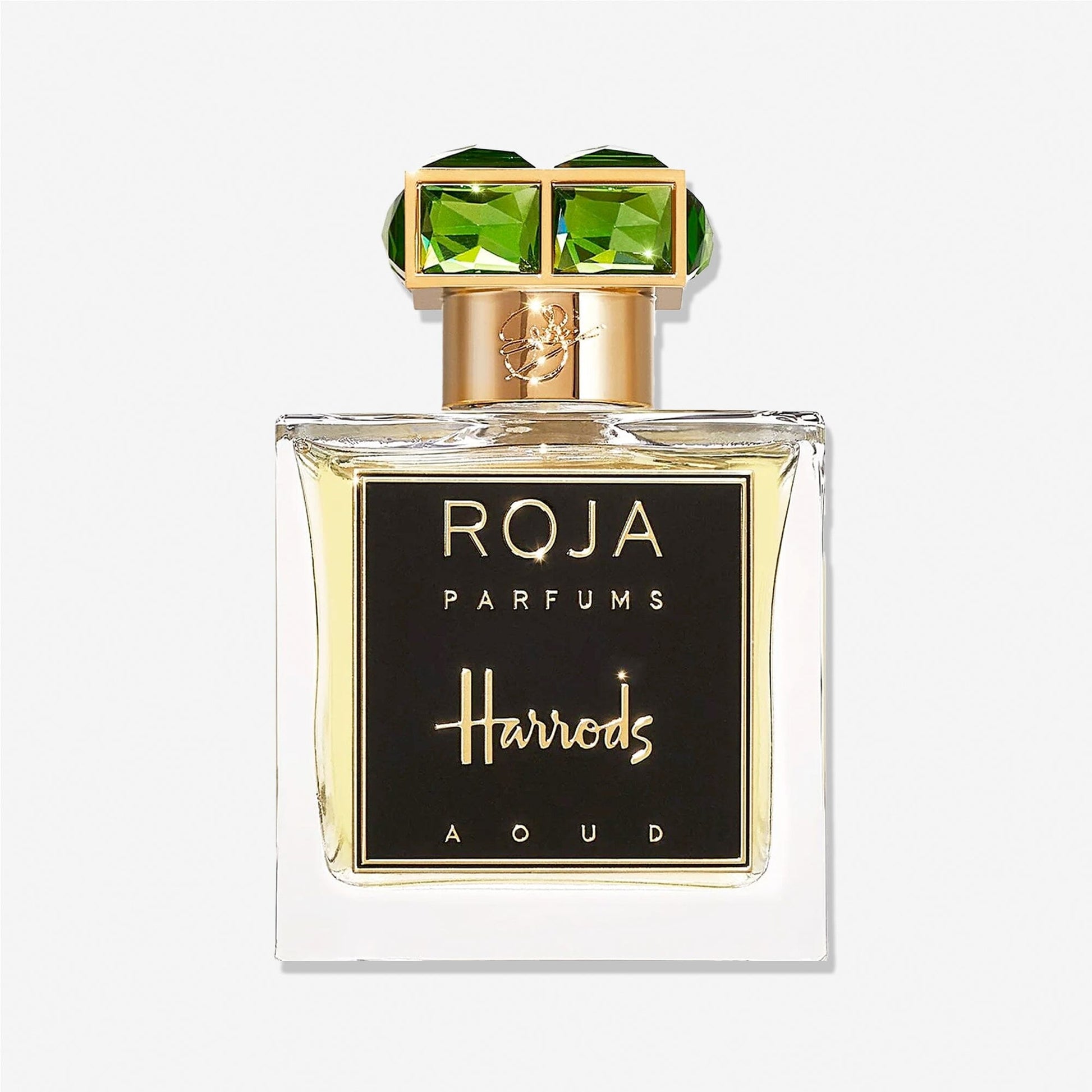 A bottle of Roja Parfums Harrods Aoud perfume features a gold cap with two large green gems and a black and gold label, embodying luxury fragrance.