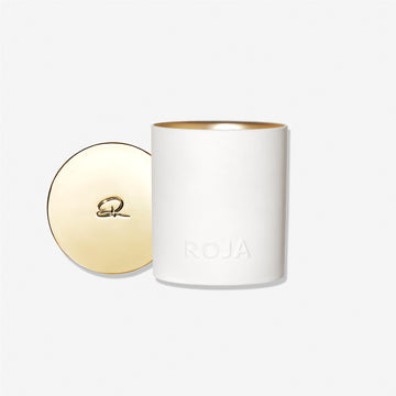 A white cylindrical London candle by Roja Parfums, embossed with ROJA, sits next to its gold-toned lid featuring an R logoâ€”reflecting Londons refined hedonismâ€”all set against a plain white background.