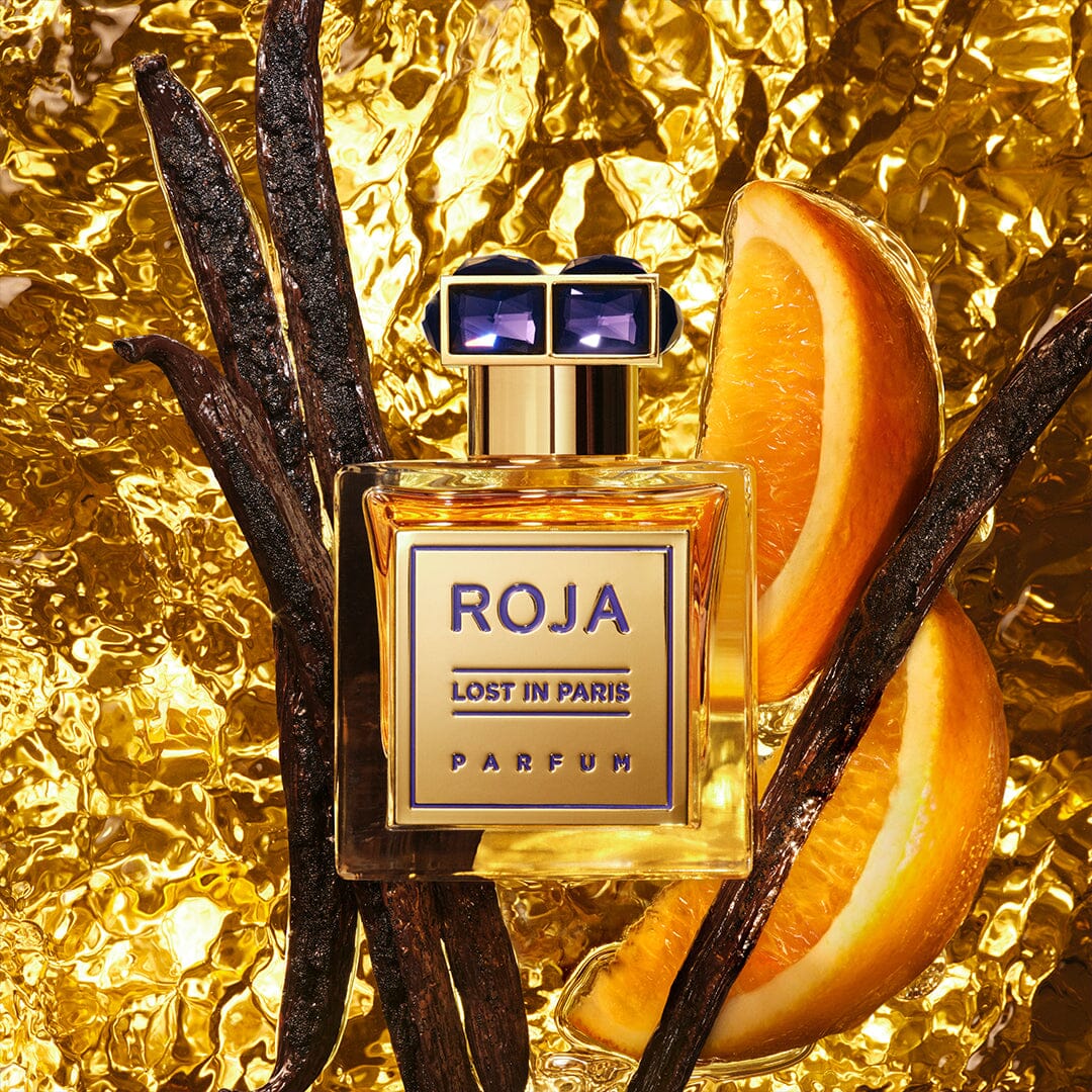 A bottle of Lost in Paris by Roja Parfums rests on gold foil, encircled by vanilla pods and orange slices, with a radiant golden background that suggests Parisian elegance and the richness of luxurious ingredients.