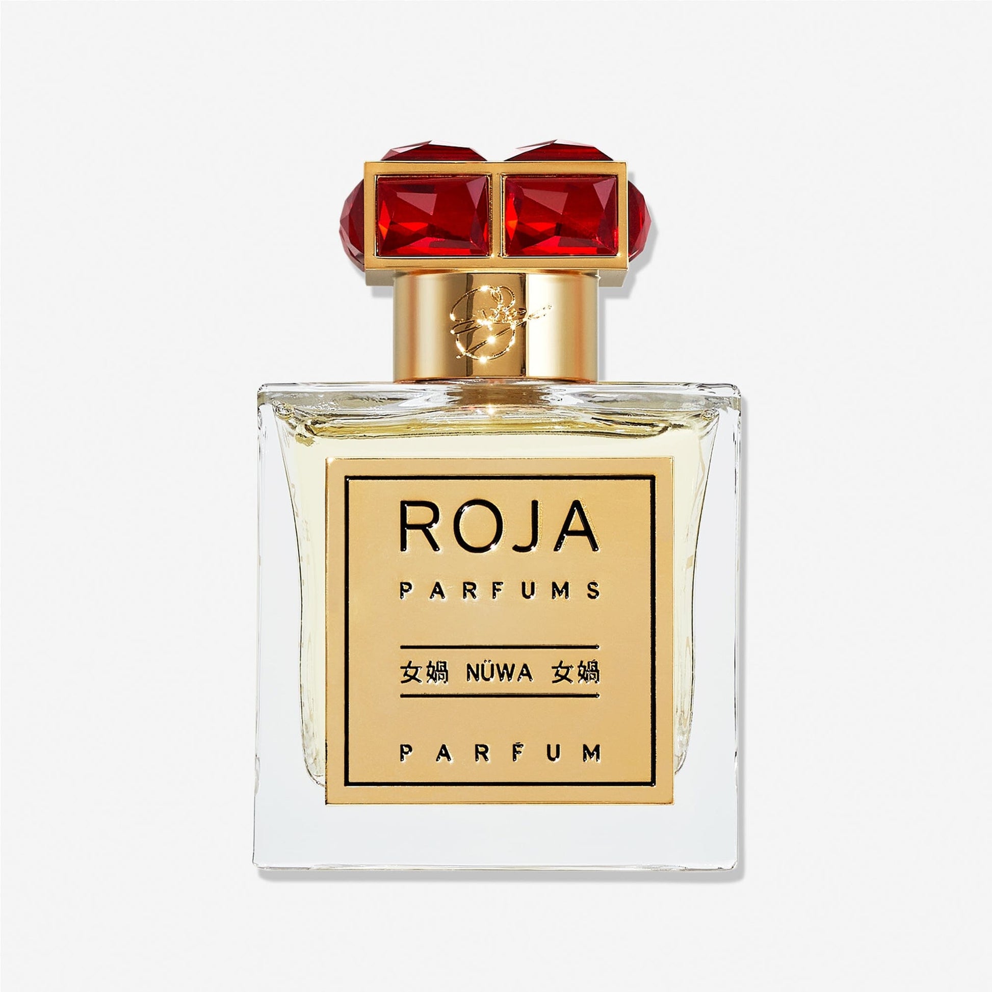 A clear glass Roja Parfums NüWa bottle with a gold label in English and Chinese, topped with a gold cap featuring two large red gemstones, reflects the warm richness of sandalwood inside.