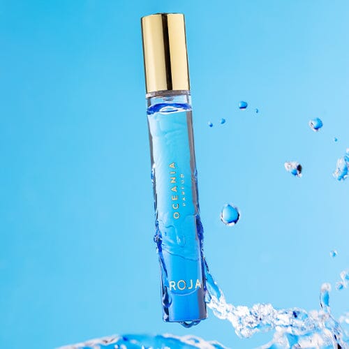 A blue bottle of Oceania by Roja Parfums stands upright with water splashing around it against a vivid blue backdrop, capturing the fresh, vibrant essence inspired by olfactive islands.