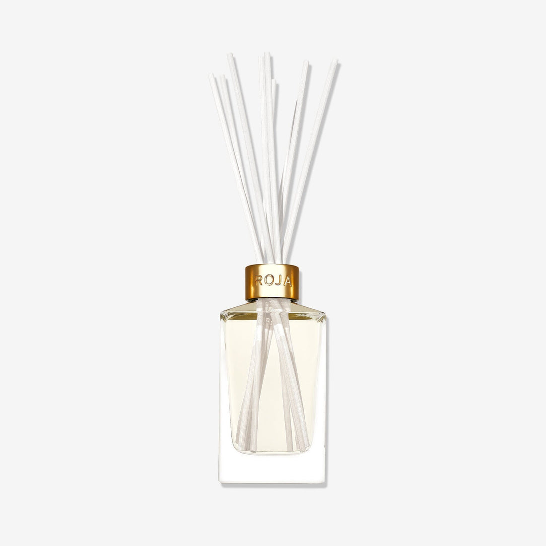 The Tea Time In The Conservatory reed diffuser by Roja Parfums features a clear glass vessel with a gold cap, light-hued liquid, and white reeds fanning out, evoking the subtle scent of Jasmine Tea against a plain white background.