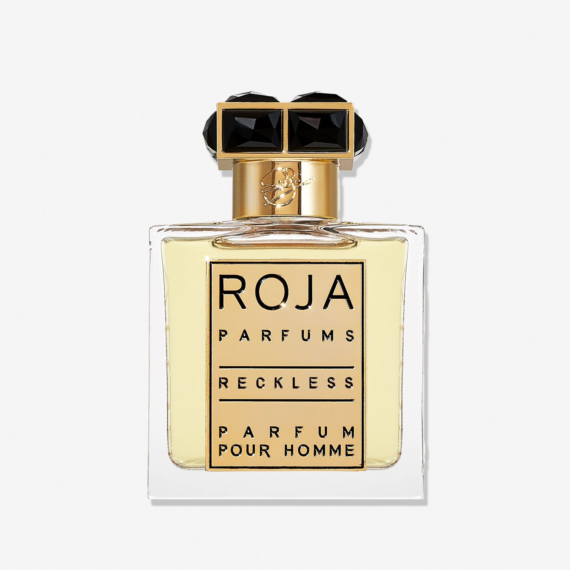 A clear glass bottle of Roja Parfums Reckless Pour Homme features a gold and black cap and holds light yellow liquid. The label shows the brand and product name in bold black lettersâ€”a masculine scent with spicy chyprÃ© notes.