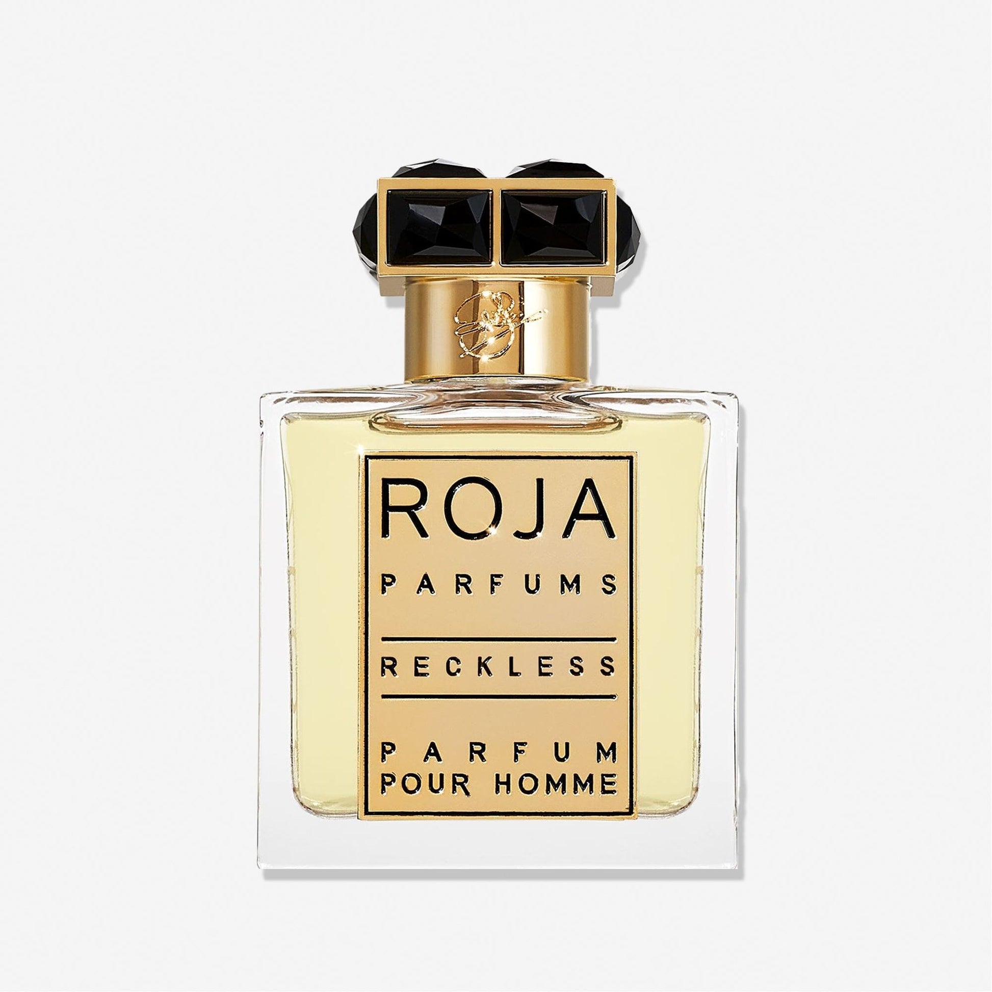 A clear glass bottle of Roja Parfums Reckless Pour Homme features a gold and black cap and holds light yellow liquid. The label shows the brand and product name in bold black lettersâ€”a masculine scent with spicy chyprÃ© notes.