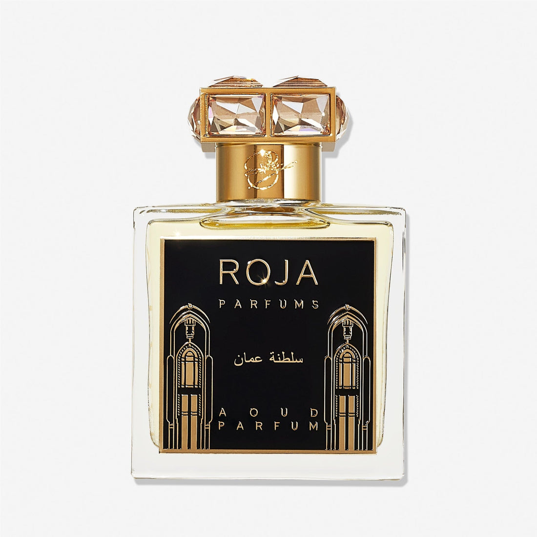A clear perfume bottle labeled Roja Parfums Sultanate of Oman features gold accents, a black and gold label with Arabic designs, and a crystal-embellished gold capâ€”evoking luxurious Aoud and smoky frankincense.
