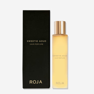 A matte black box labeled Sweetie Aoud Hair Perfume by Roja Parfums sits beside a frosted bottle with a gold cap and gold text, both on a plain white background—showcasing this luxurious gourmand perfume with rich agarwood notes.