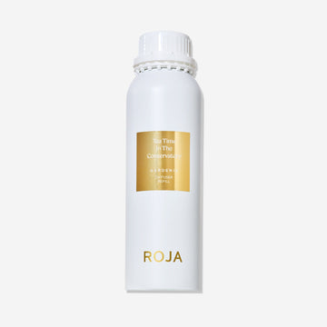 A white cylindrical bottle with a white cap and gold label displays "Tea Time In The Conservatory" by Roja Parfums, evoking the charm of an English country garden and the elegance of afternoon tea.