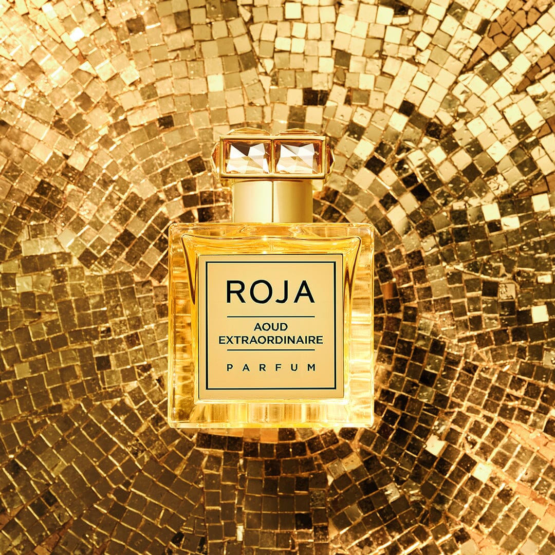 A bottle from Roja Parfums’ The Aoud Layering Gift Set is showcased against a sparkling golden mosaic, emphasizing the opulent allure of oud and adding a glamorous touch.