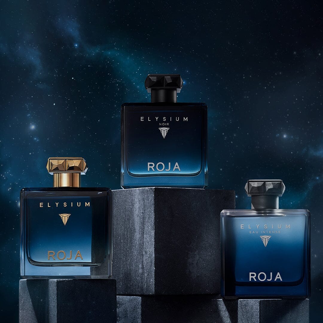Three blue bottles from The Elysium Trio by ROJA London sit on dark stone against a starry night sky, each with gold or black accents and ROJA in gold—an elegant choice to enhance your fragrance wardrobe and Art Of Layering ritual.